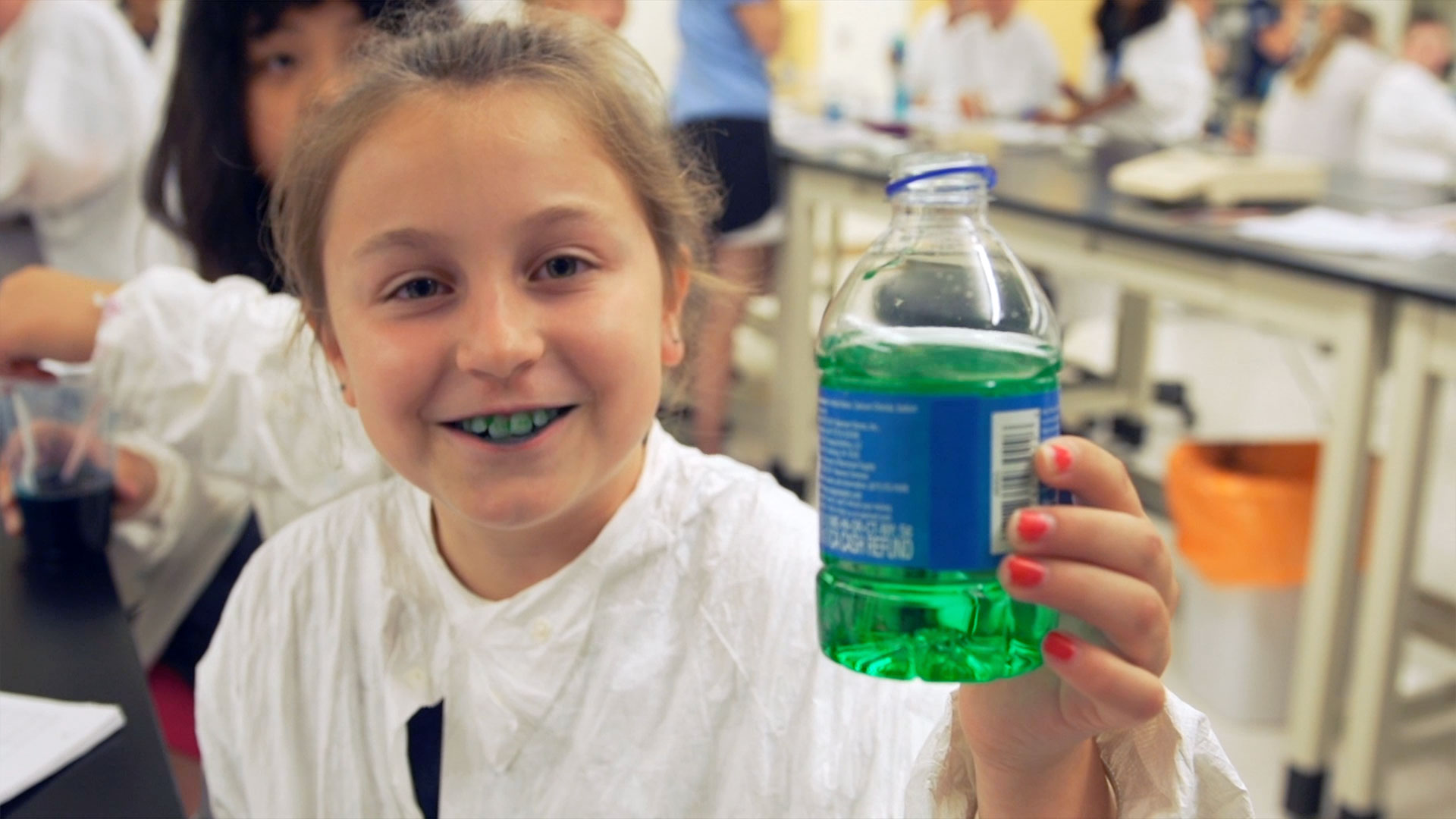 Young girl shows water bottle dyed green from the food coloring in her mouth