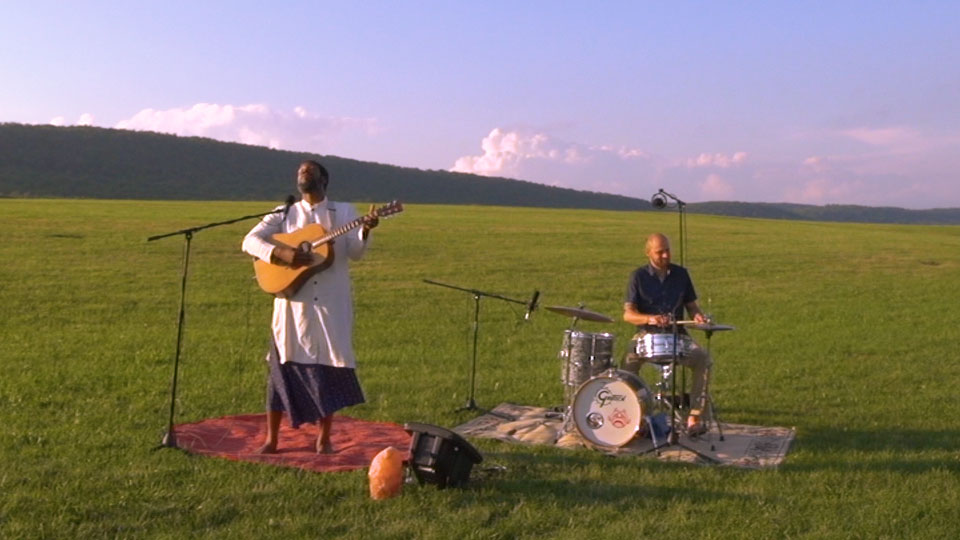 Guitar player and drummer performing in an open grass field