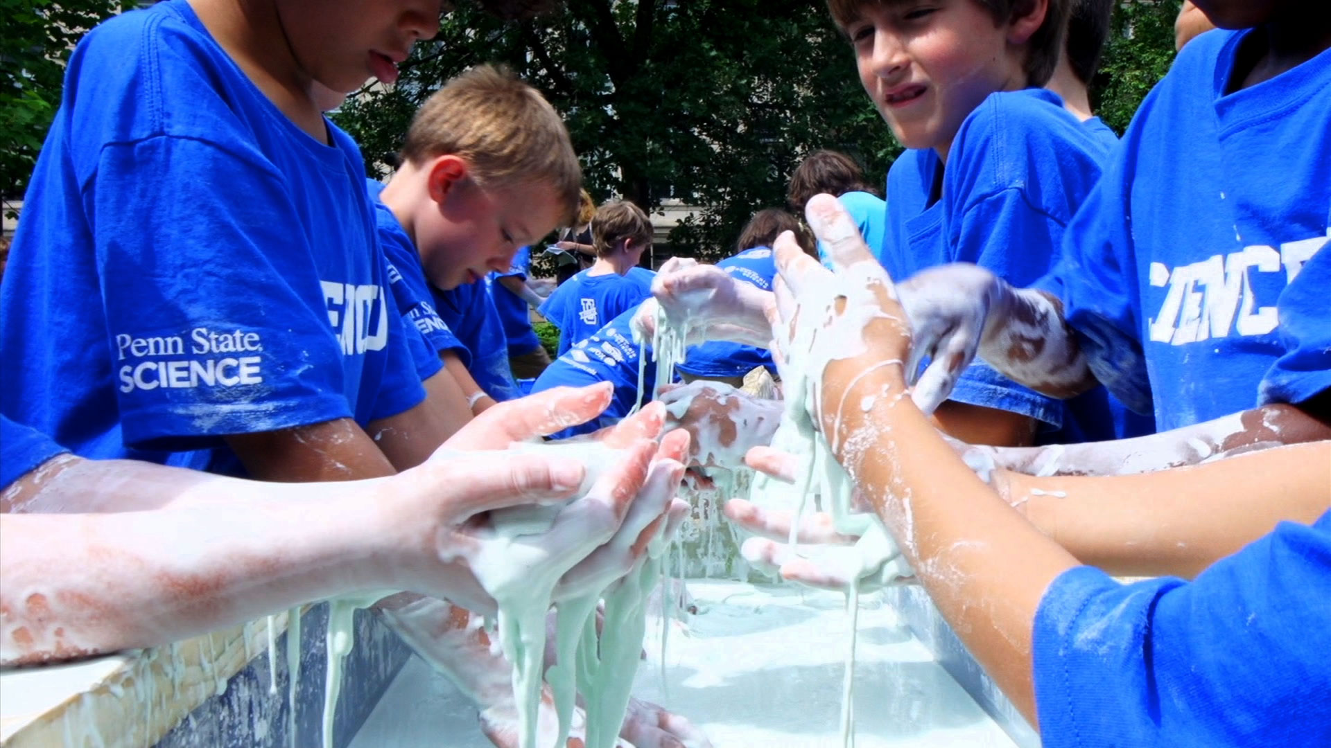 Several young students putting their hands in a mixture of corn starch and water