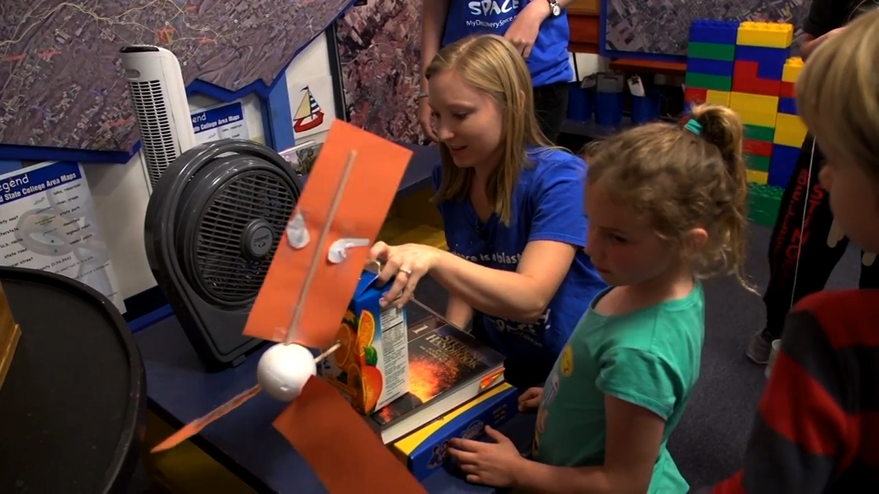 Young adult female assisting grade school child with science experiement