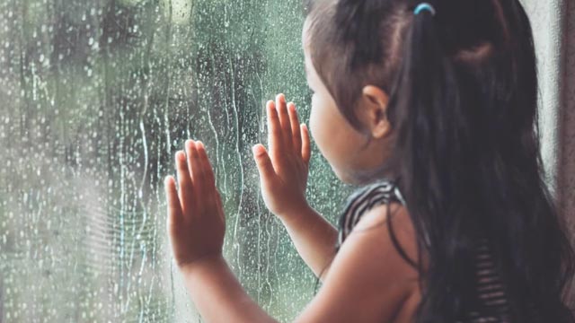 young girl watching rain through window