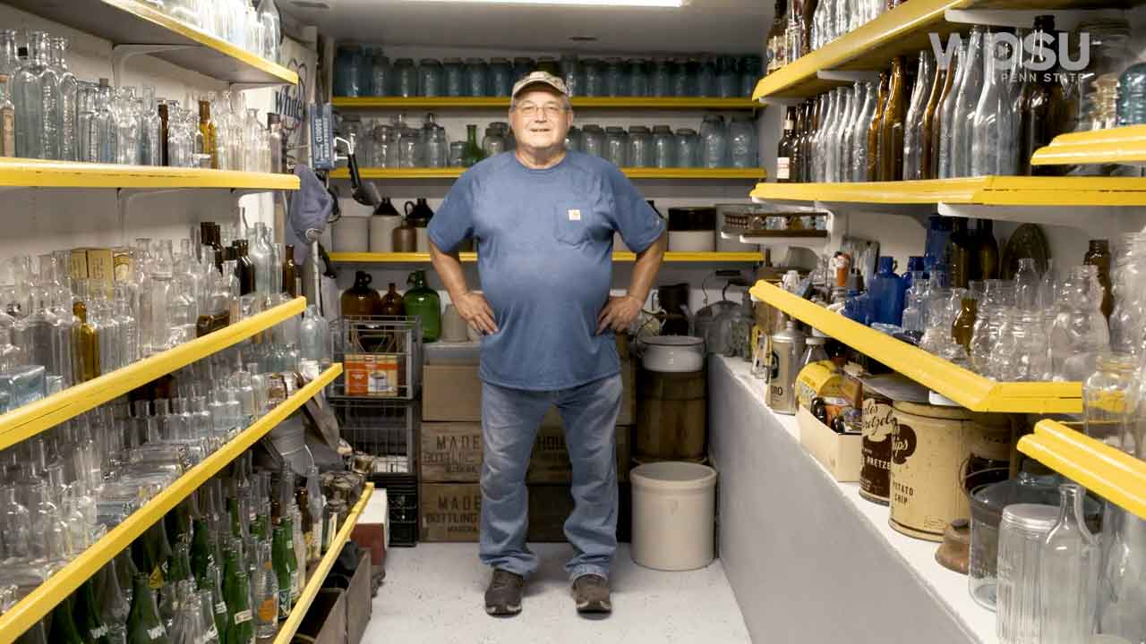 Person standing surrounded by shelves filled with antique bottles