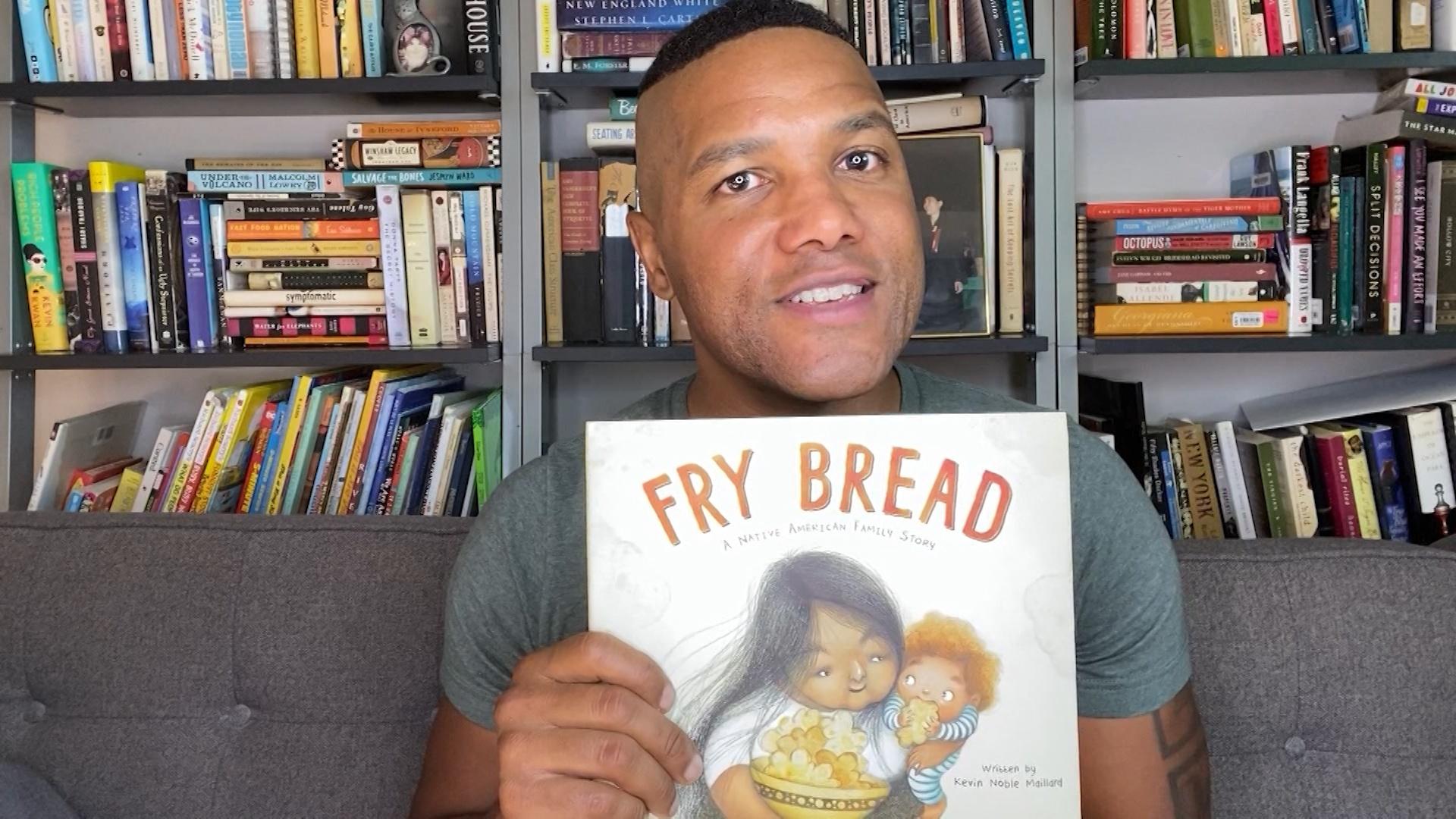 A man holding a children's book titled "Fry Bread"