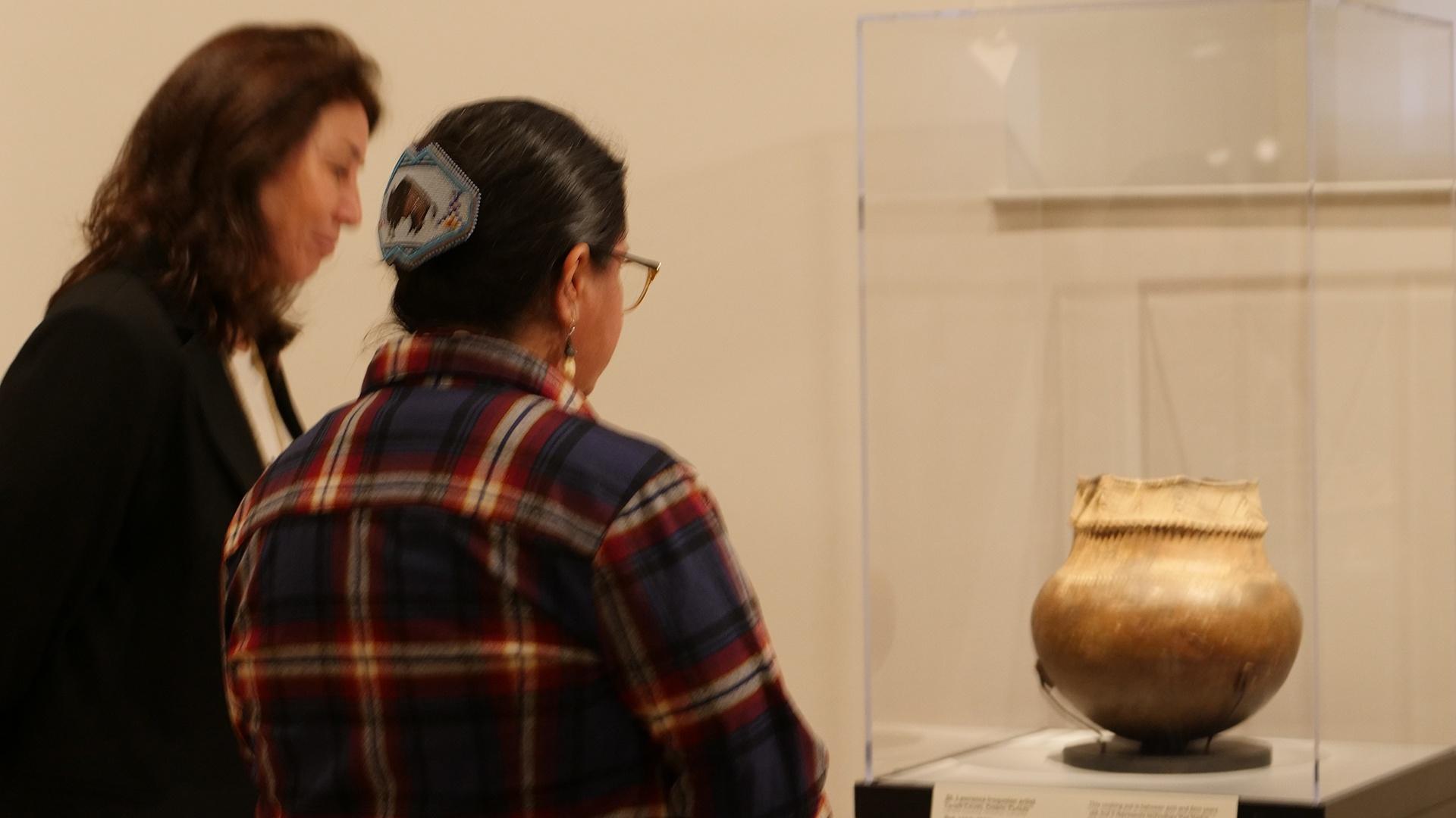 Two women standing in front a pot in a museum display