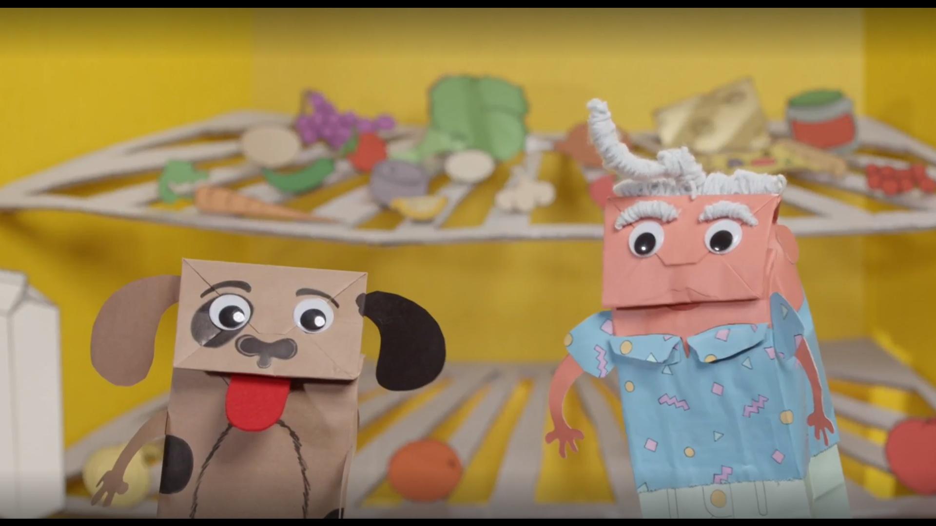 Two paper bag puppets standing in front of refrigerator shelves
