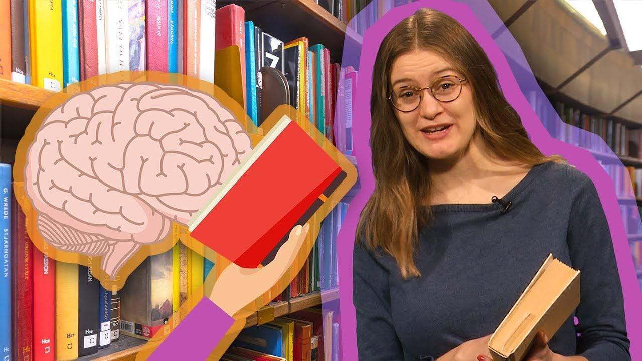 A girl with glasses holding a book and standing next to a drawing of a brain reading a book