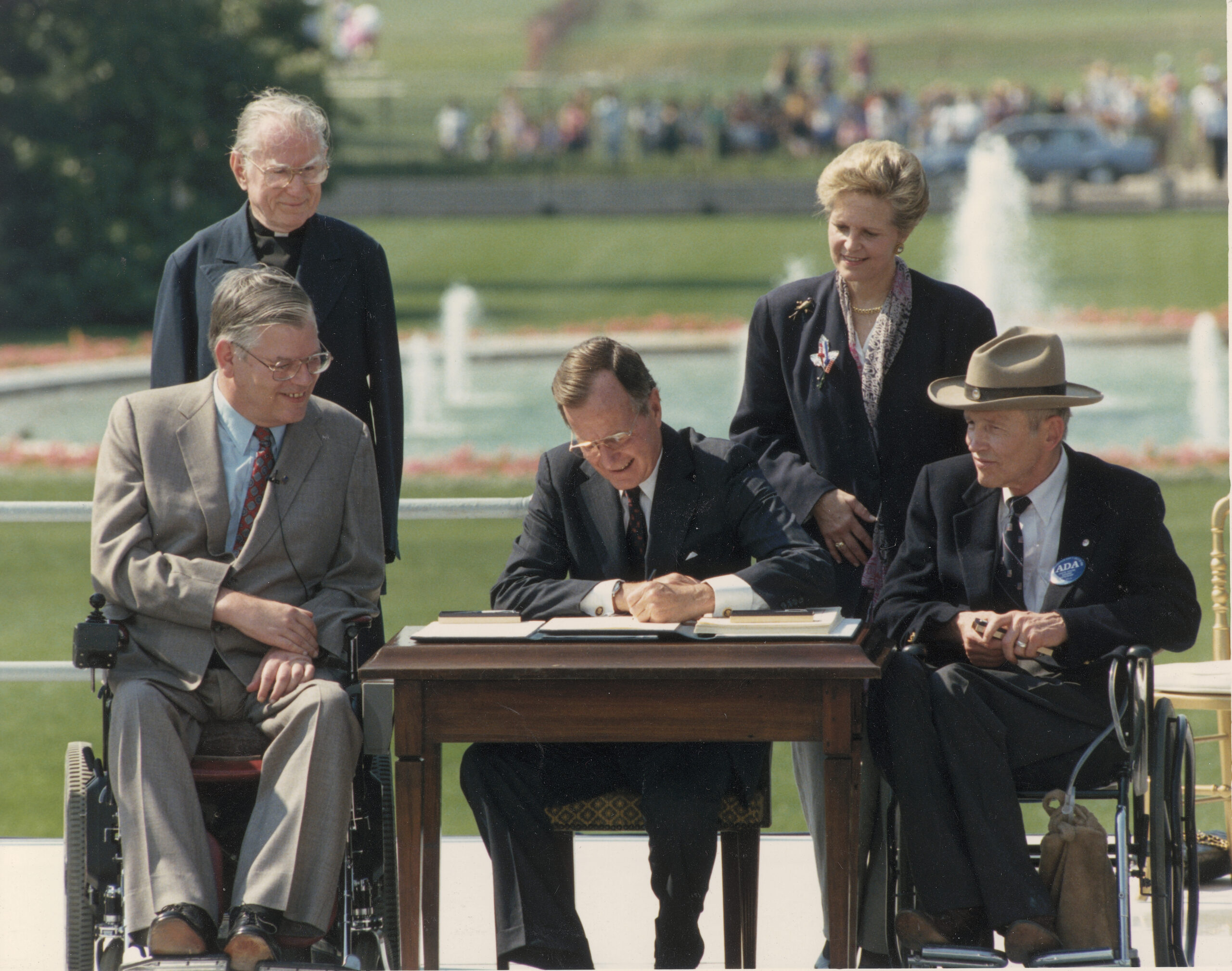 Two men in wheelchairs on either side of President George H. W. Bush signing the ADA into law.