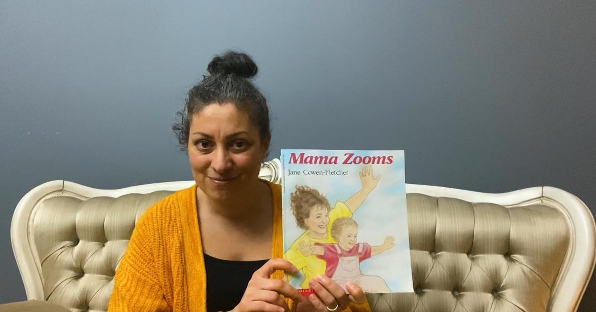 A woman holding a children's book titled "Mama Zooms".