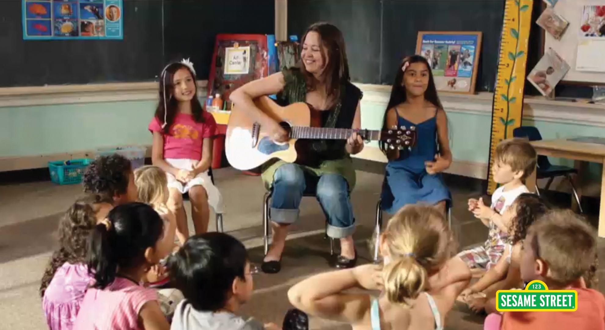 A woman with a guitar singing with a class of children.