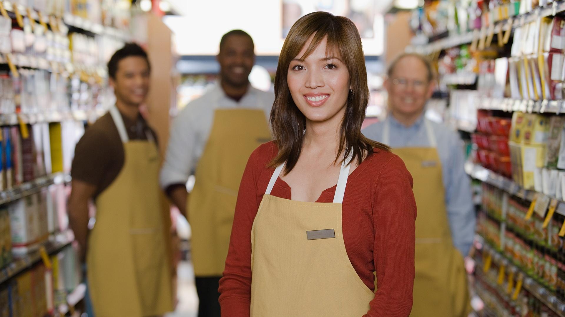 One woman standing in front of three mean all wearing aprons