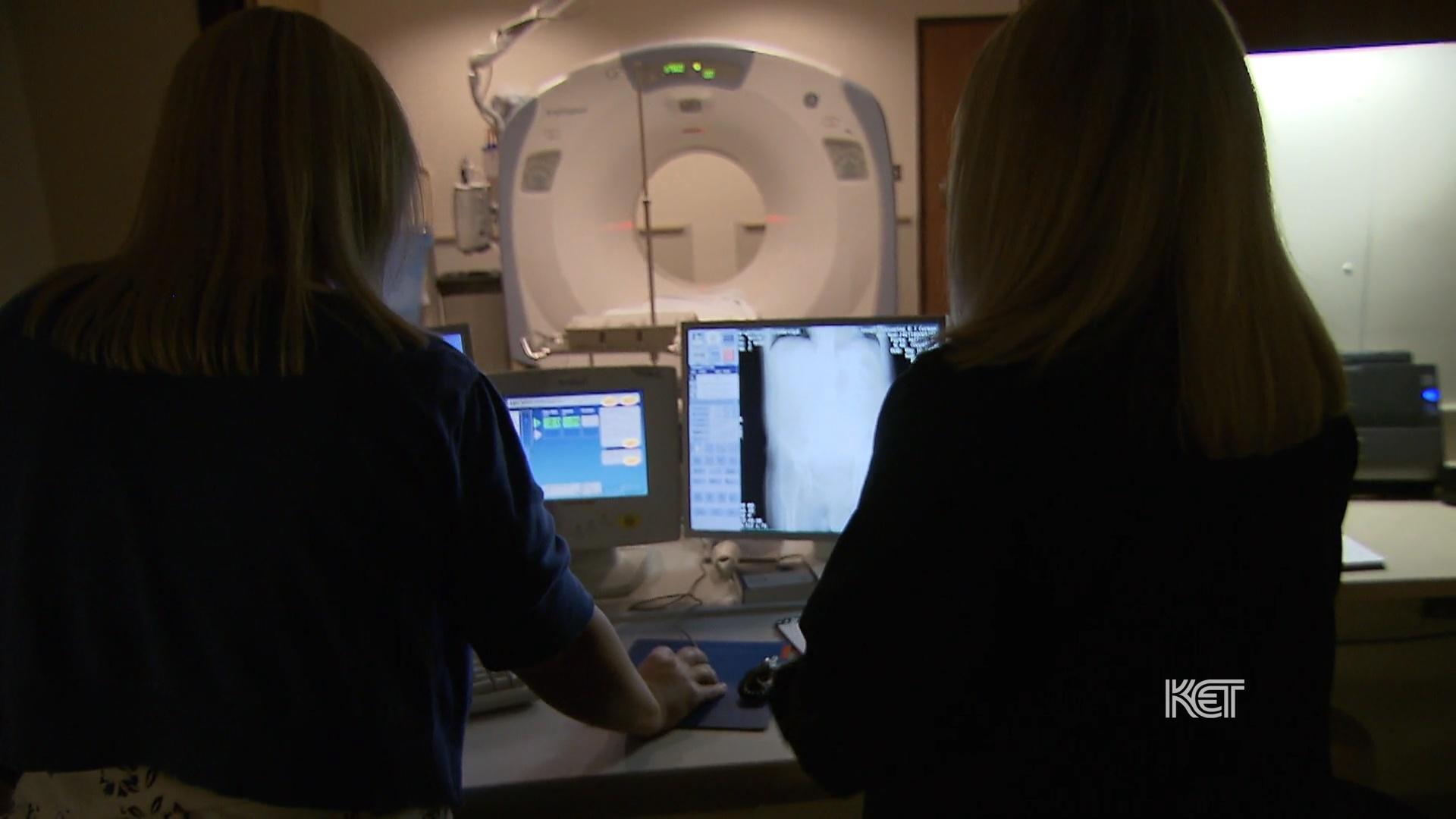 Two women standing in front of computers and an MRI machine
