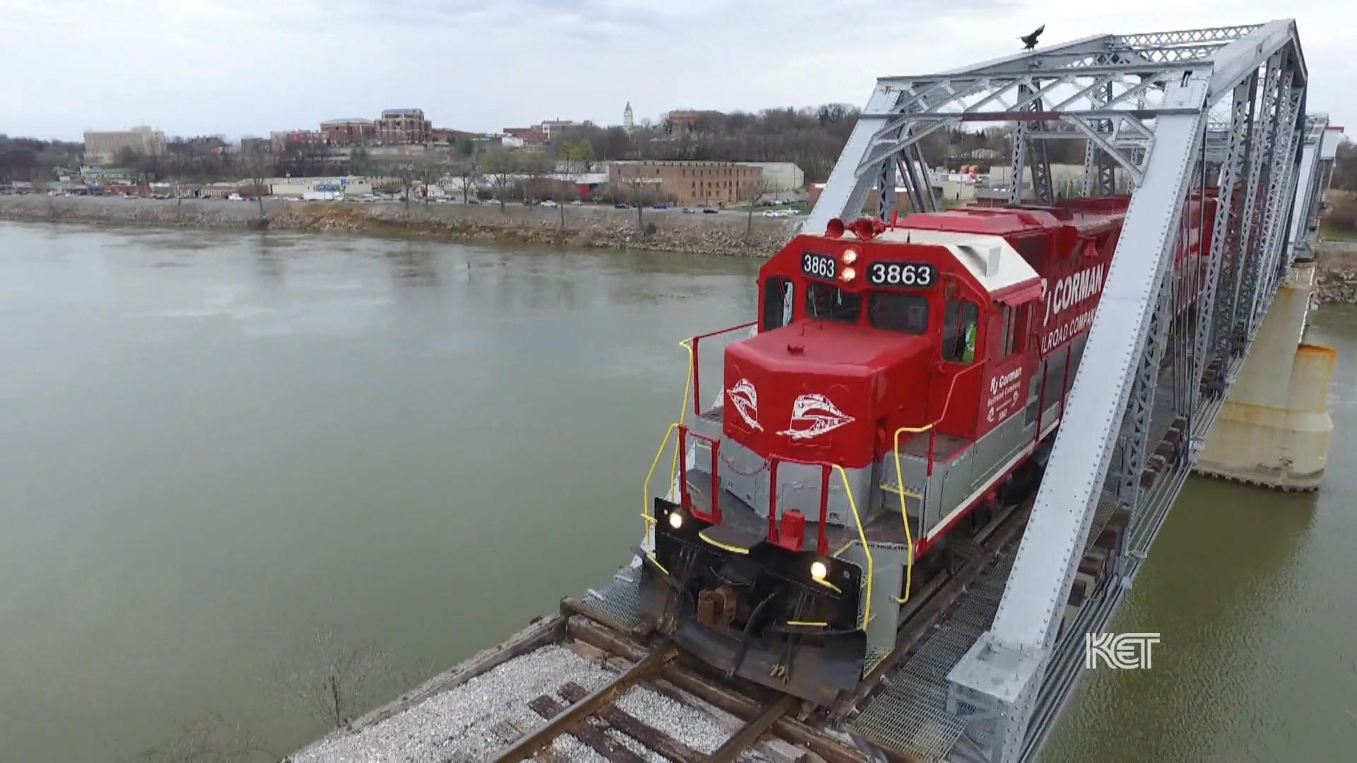 A red train riding on a steel bridge over a river
