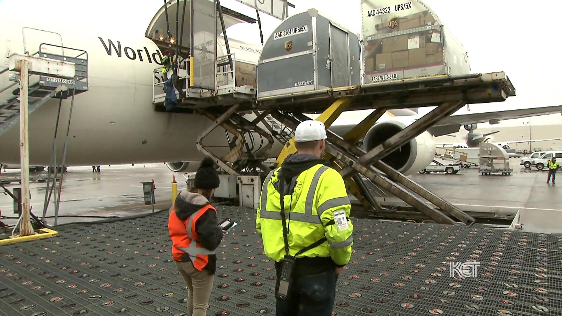 Two people in safety vests standing in front of a cargo plane.