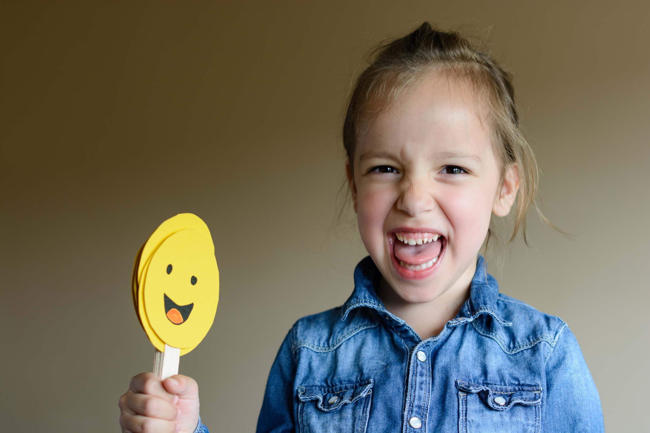 A girl smiling holding a paper face stick.