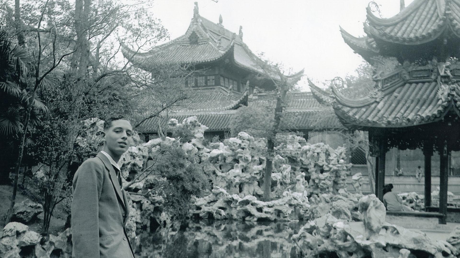 A black and white image of a man in front of a Chinese garden.