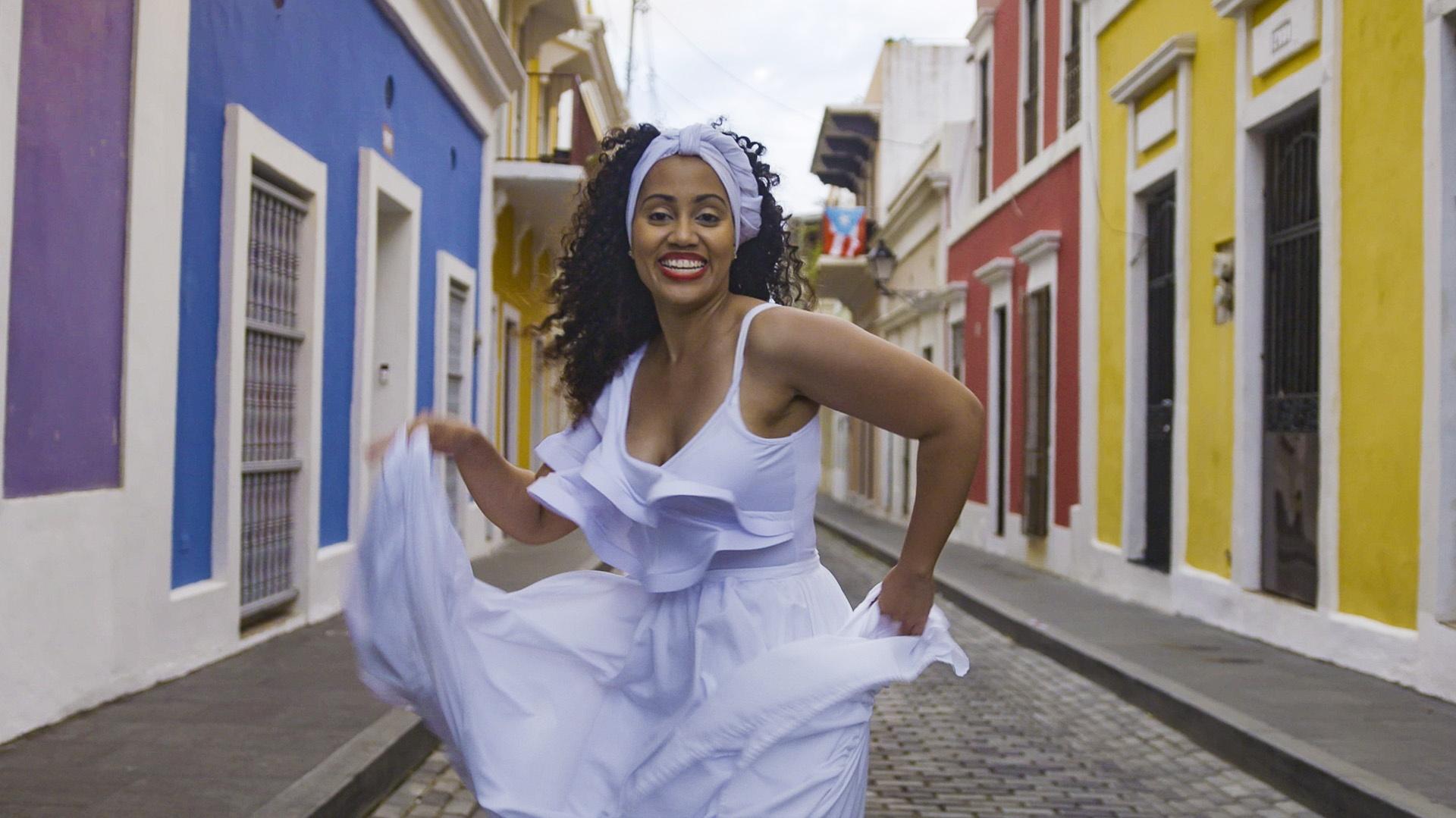 A woman in a white dress dancing the bomba in a street.