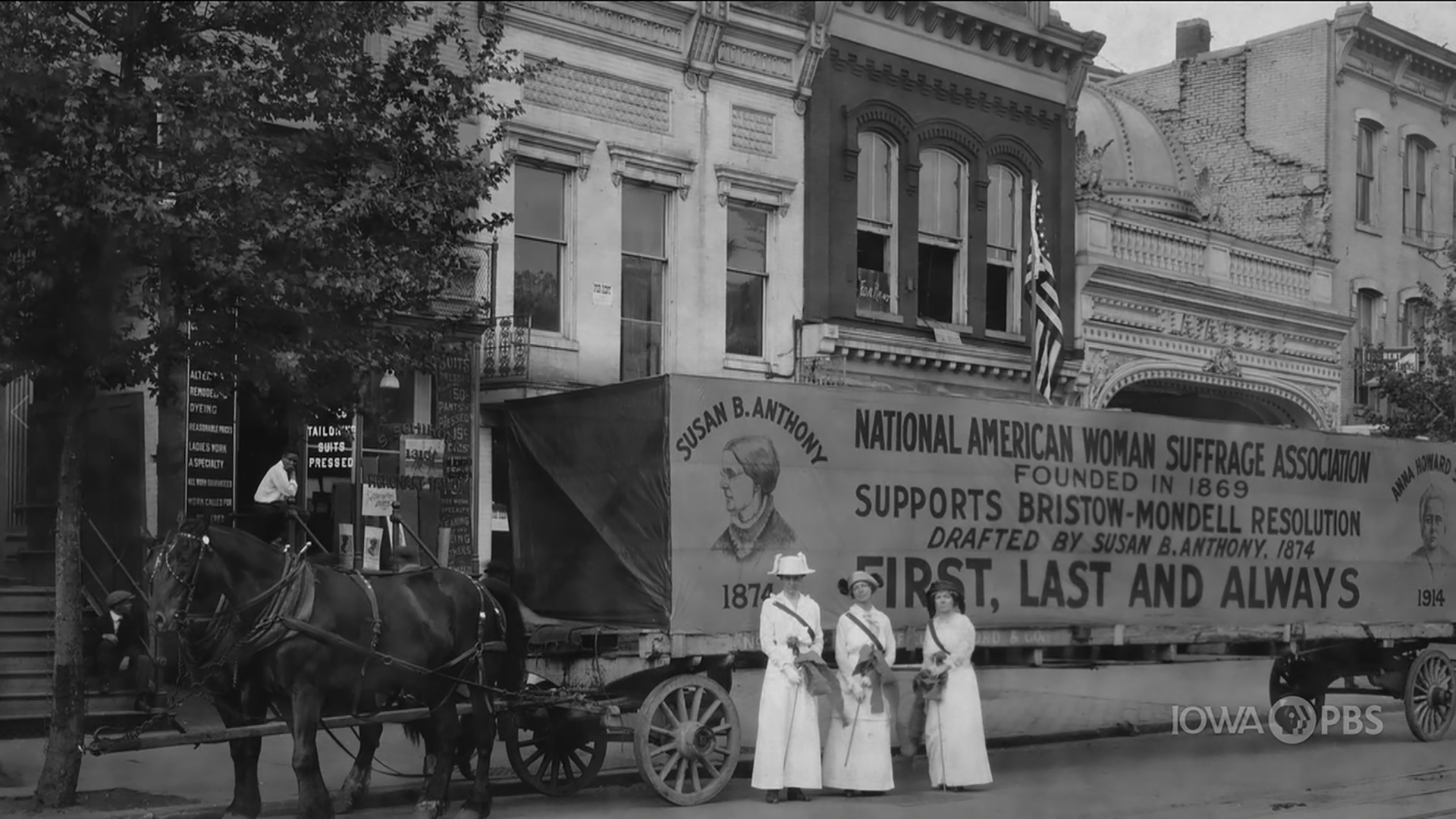 Three suffragettes standing in front of a mobile advertisement.