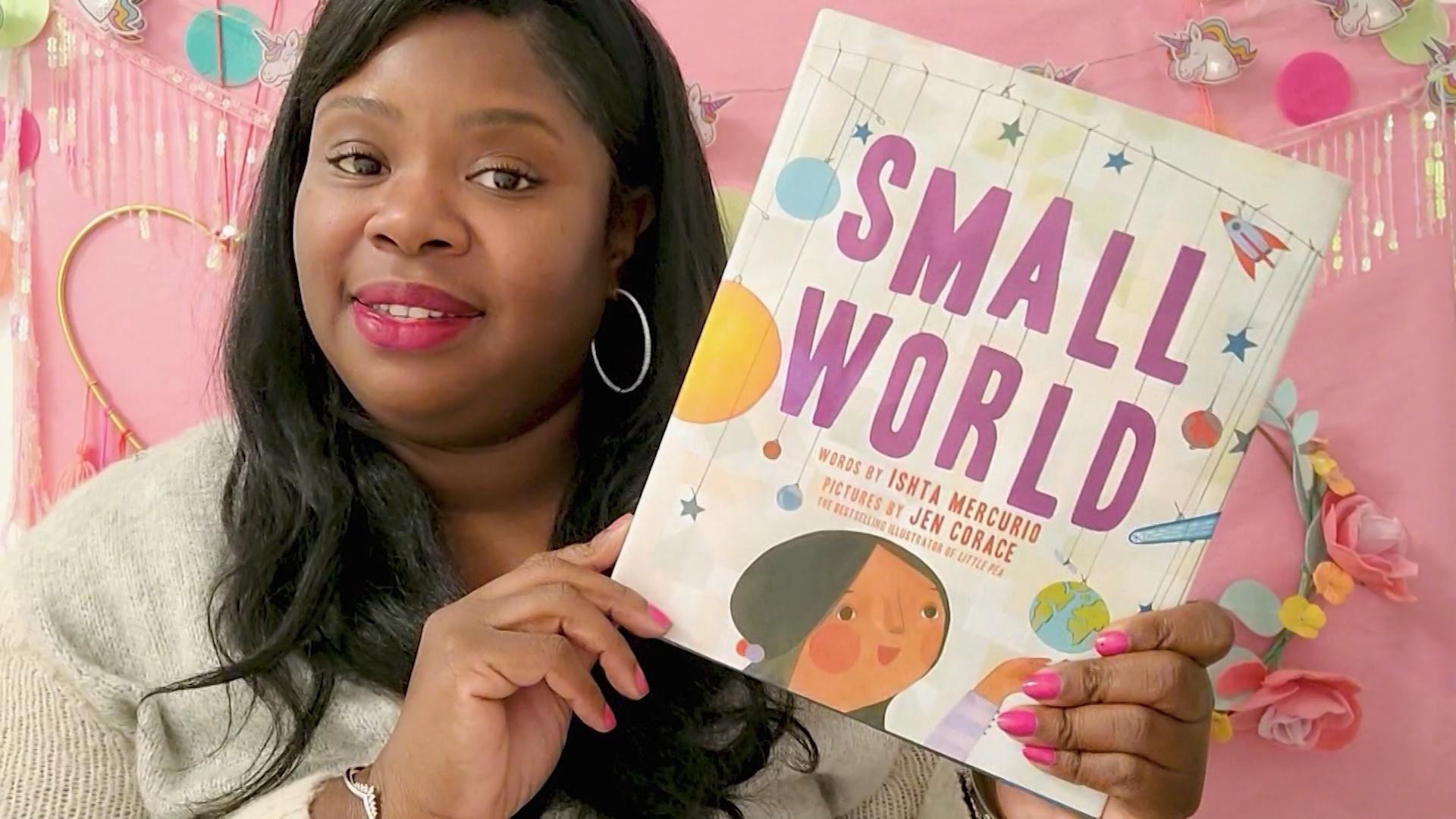 A black woman holding up a book titled "Small World."