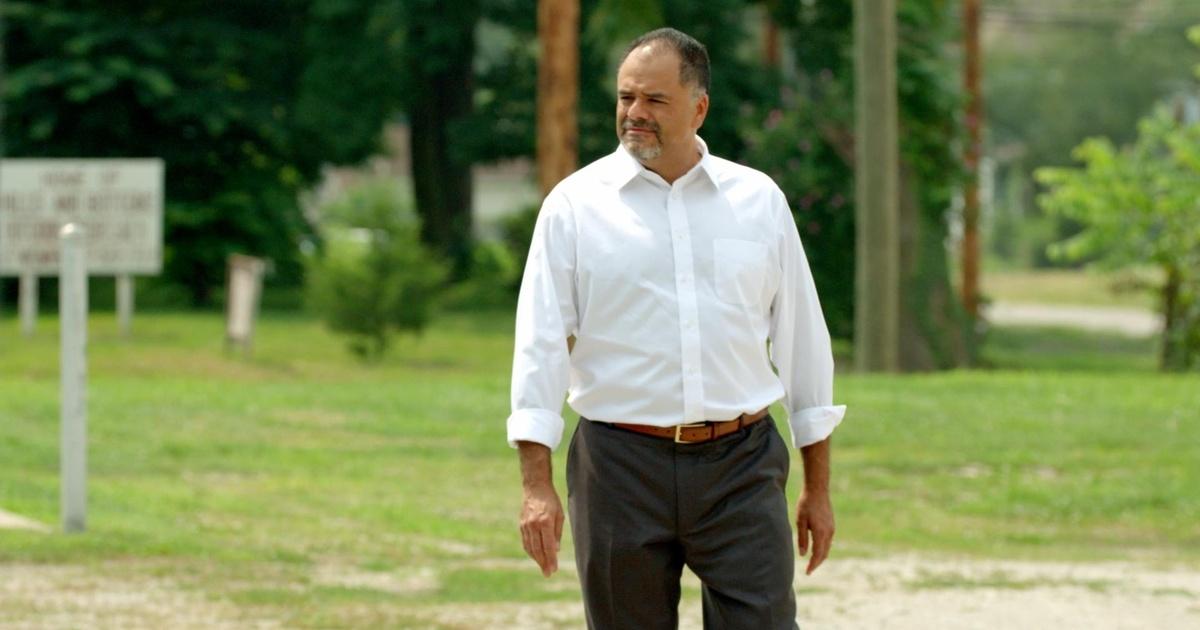 A man in a white shirt walking in a park.