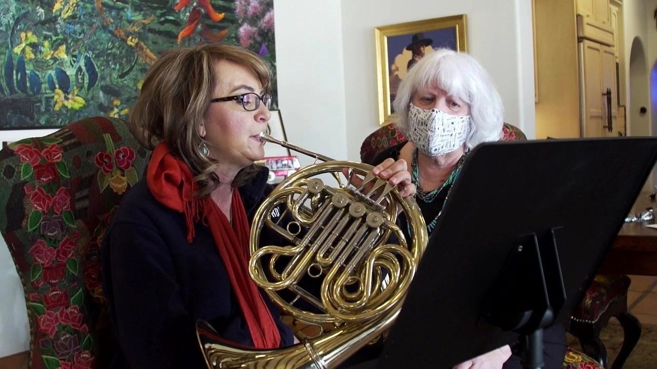 Gabby Giffords plays a french horn with a music teacher.