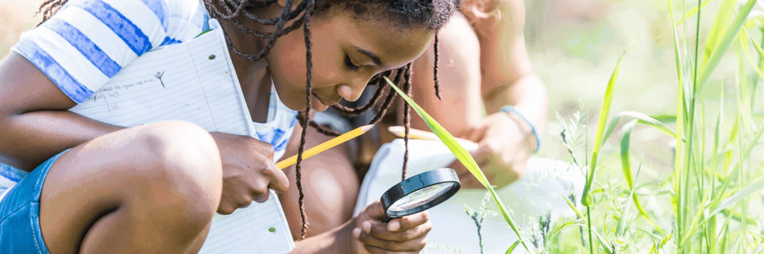 A black girl with a magnifying glass bends down to look closely at plants.