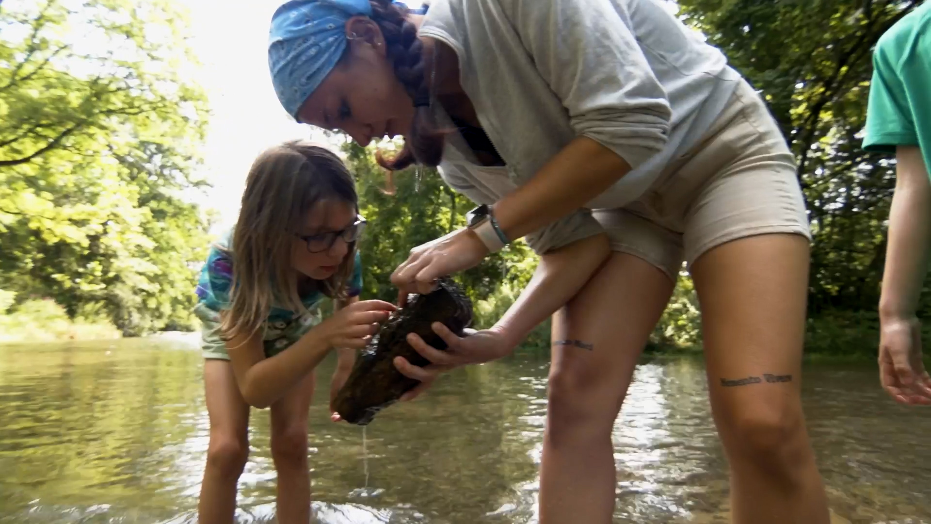 A kid and an instructor standing in a stream and conducting scientific observations.