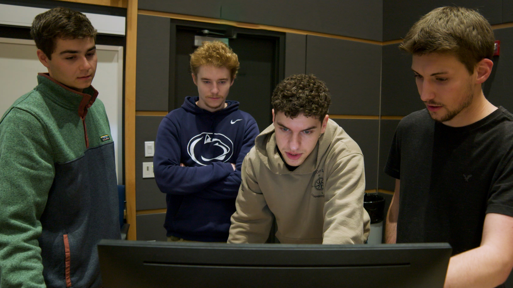 A group of four students gathered behind a computer monitor.