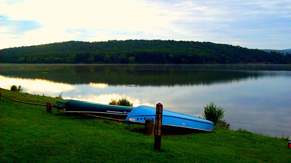 Blue canoe resting on a lake shoreline with mountains in background.