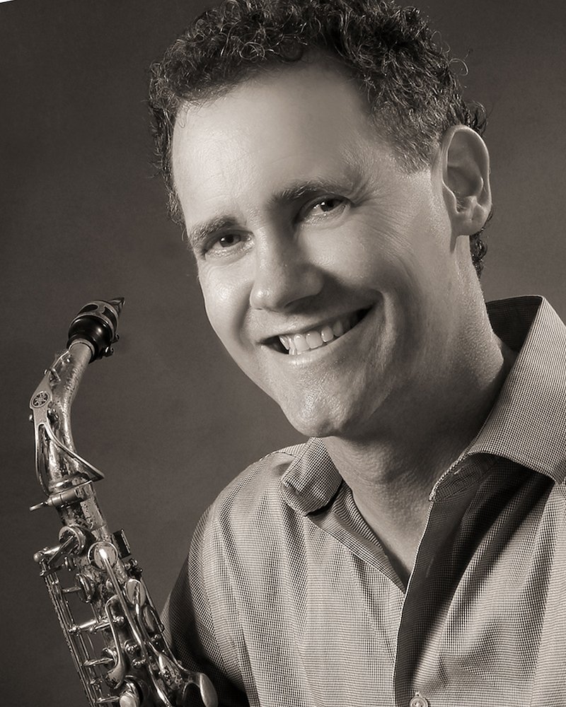 Headshot of Rick Hirsch smiling and holding a saxophone.