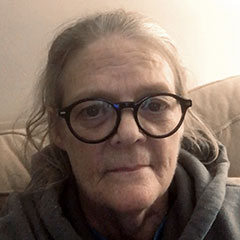 woman with gray hair and glasses in a gray hooded sweatshirt.