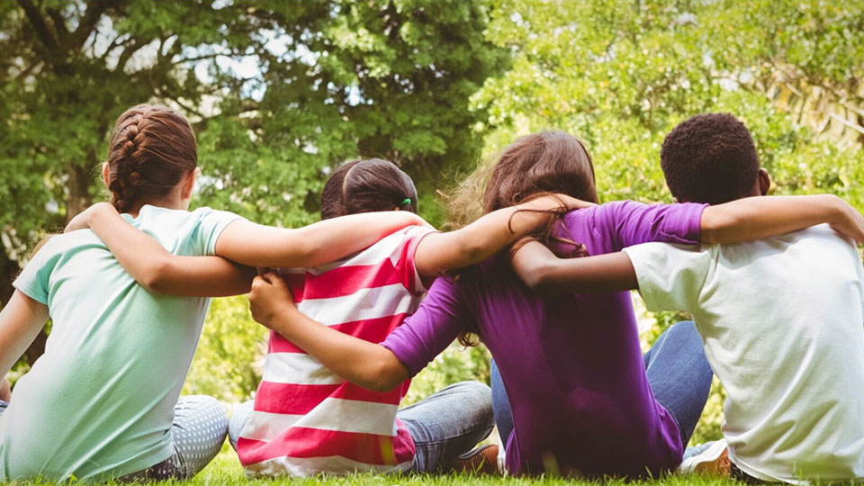 view from behind of four young people sitting with arms around each other.