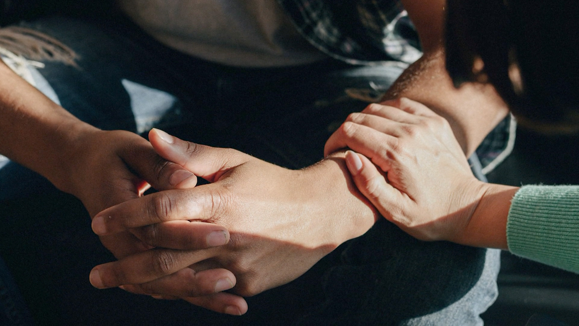 Close up of pair of male hands folded together with a female's hand reaching and embracing the male's wrist.