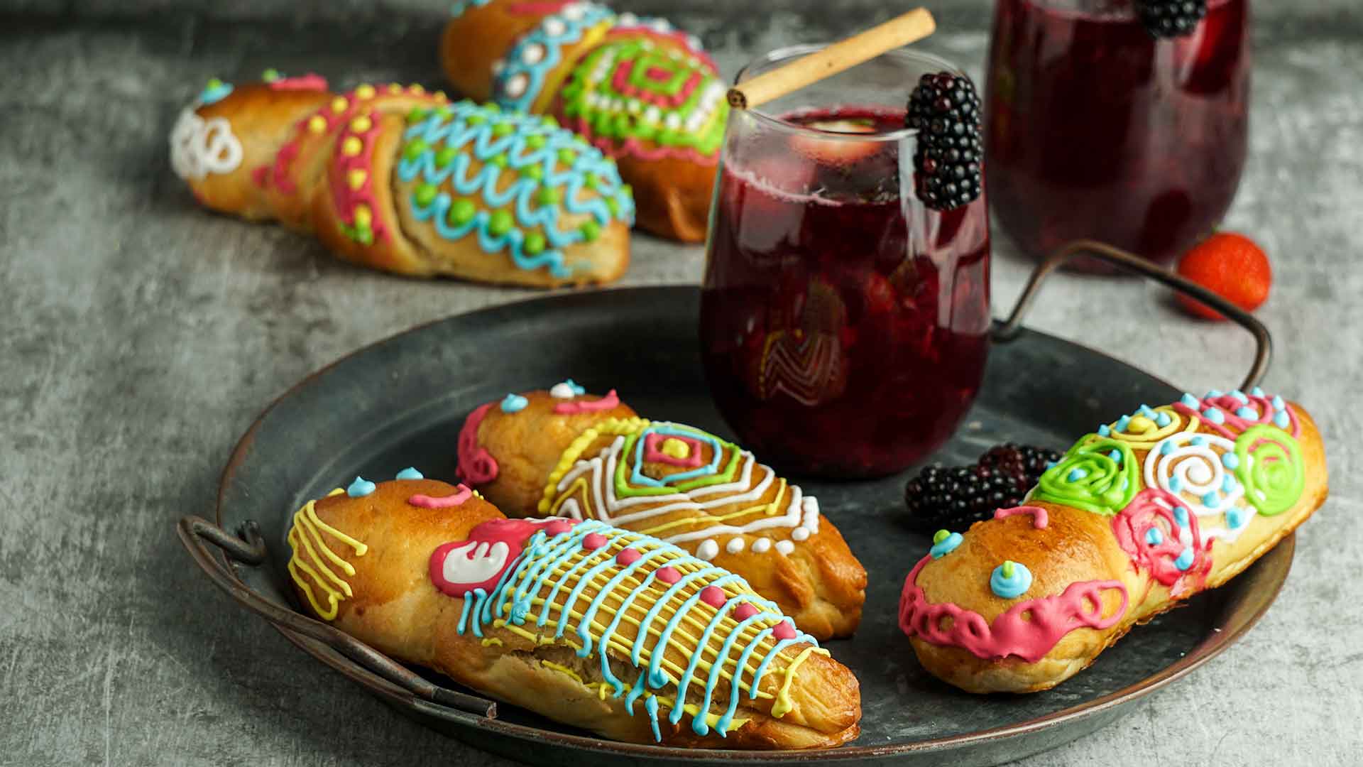 pastries decorated like dolls on a black plate along side a dark purple colored cocktail.