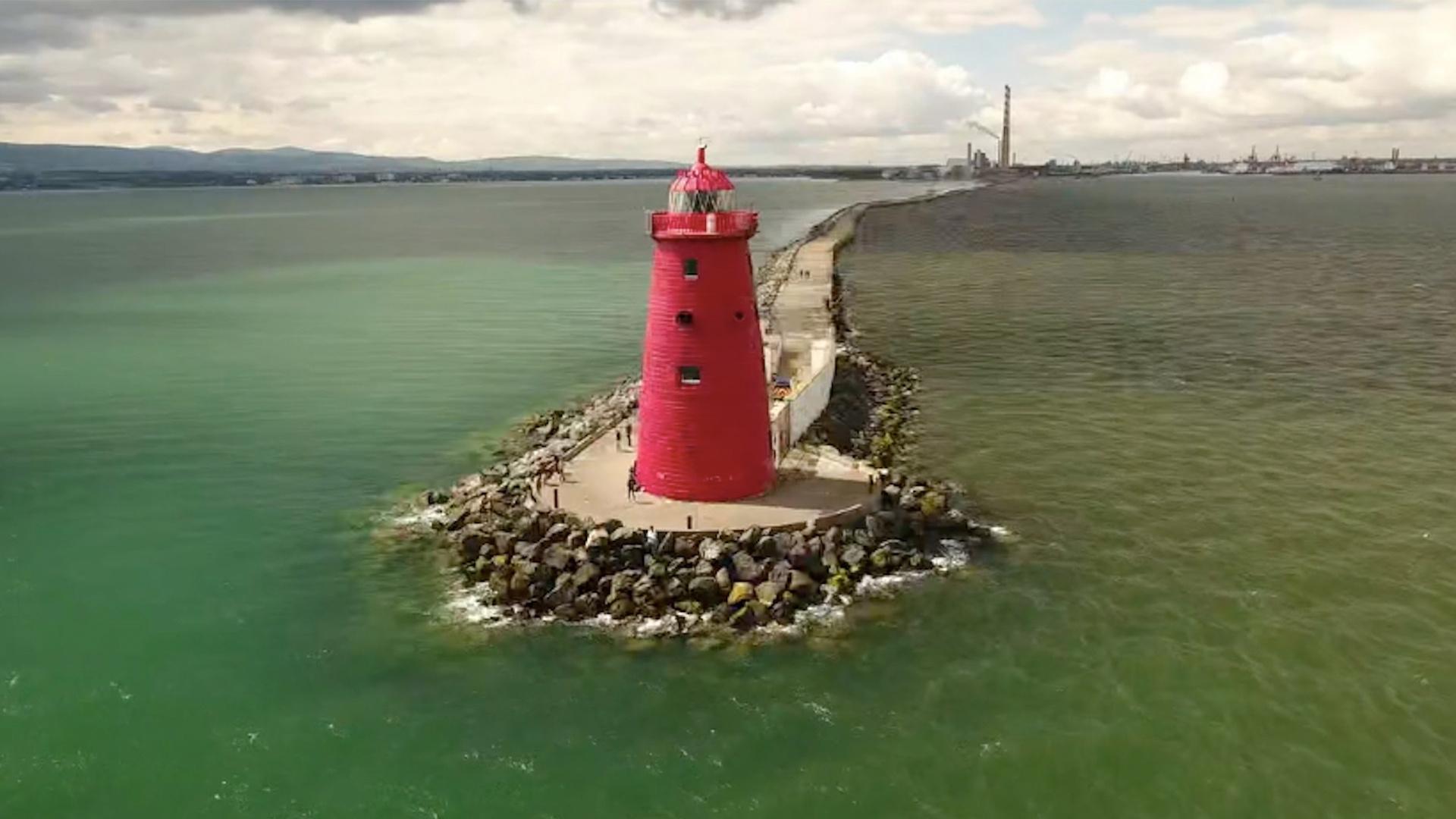 Red lighthouse on a rocky peninsula surrounded by water with greenish huel