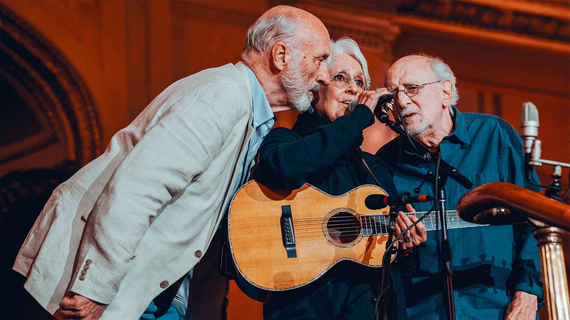 Musicians Peter, Paul, and Mary huddling around a mic stand.