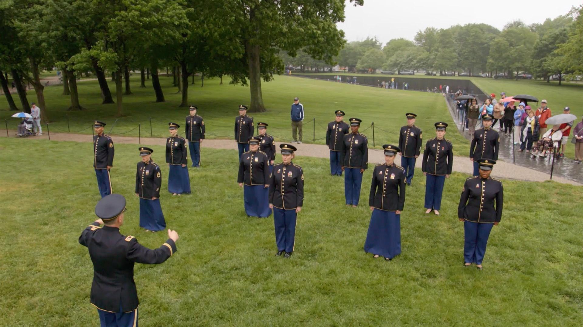 Singers in US Marine uniforms standing in a grass field.