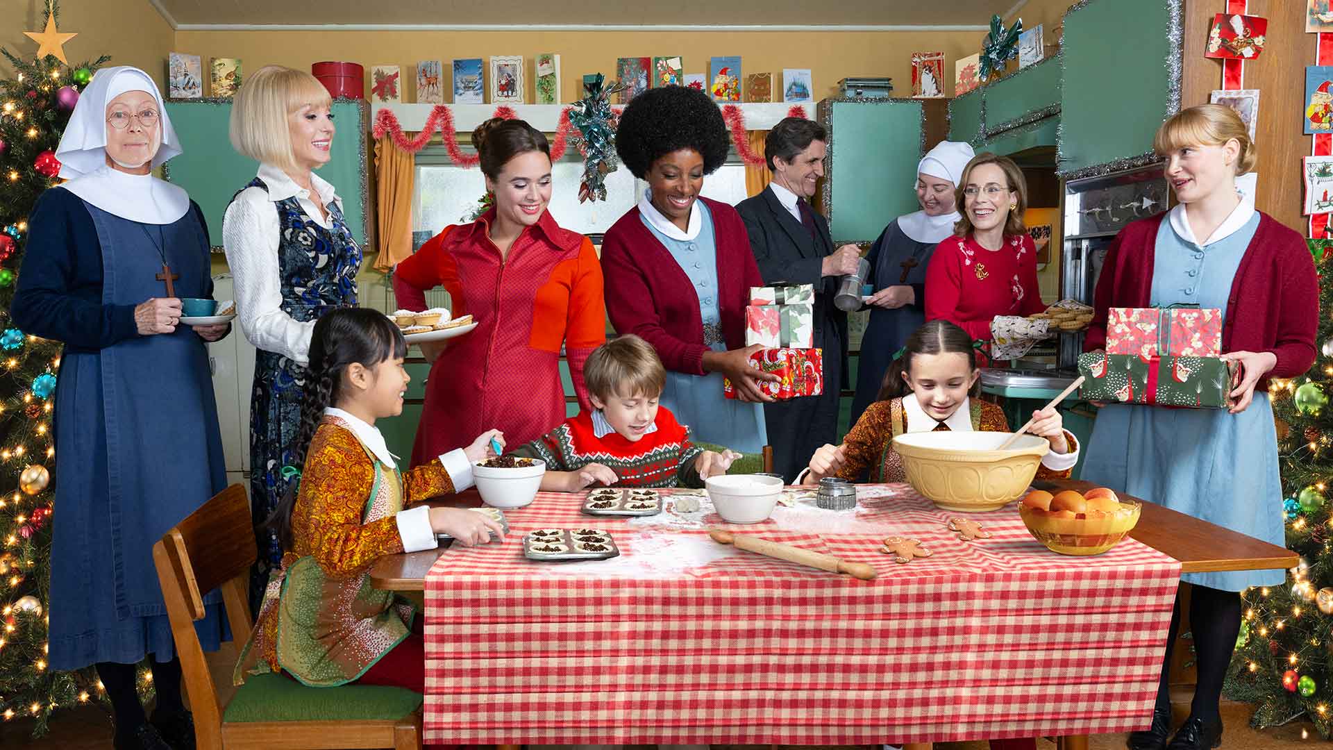 Cast of Call the Midwife around a table of food surrounded by Christmas decorations.