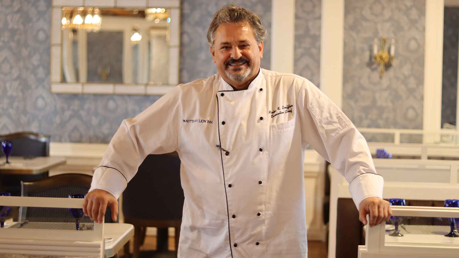 Mirko Loeffler in a white chef jacket standing in a restaurant dining room.