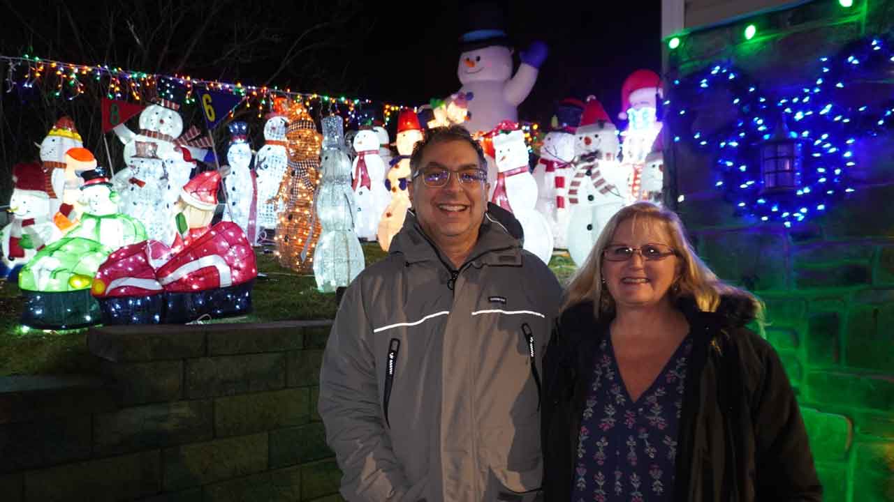 A man a woman standing infront of many lit up snowman yard decorations.