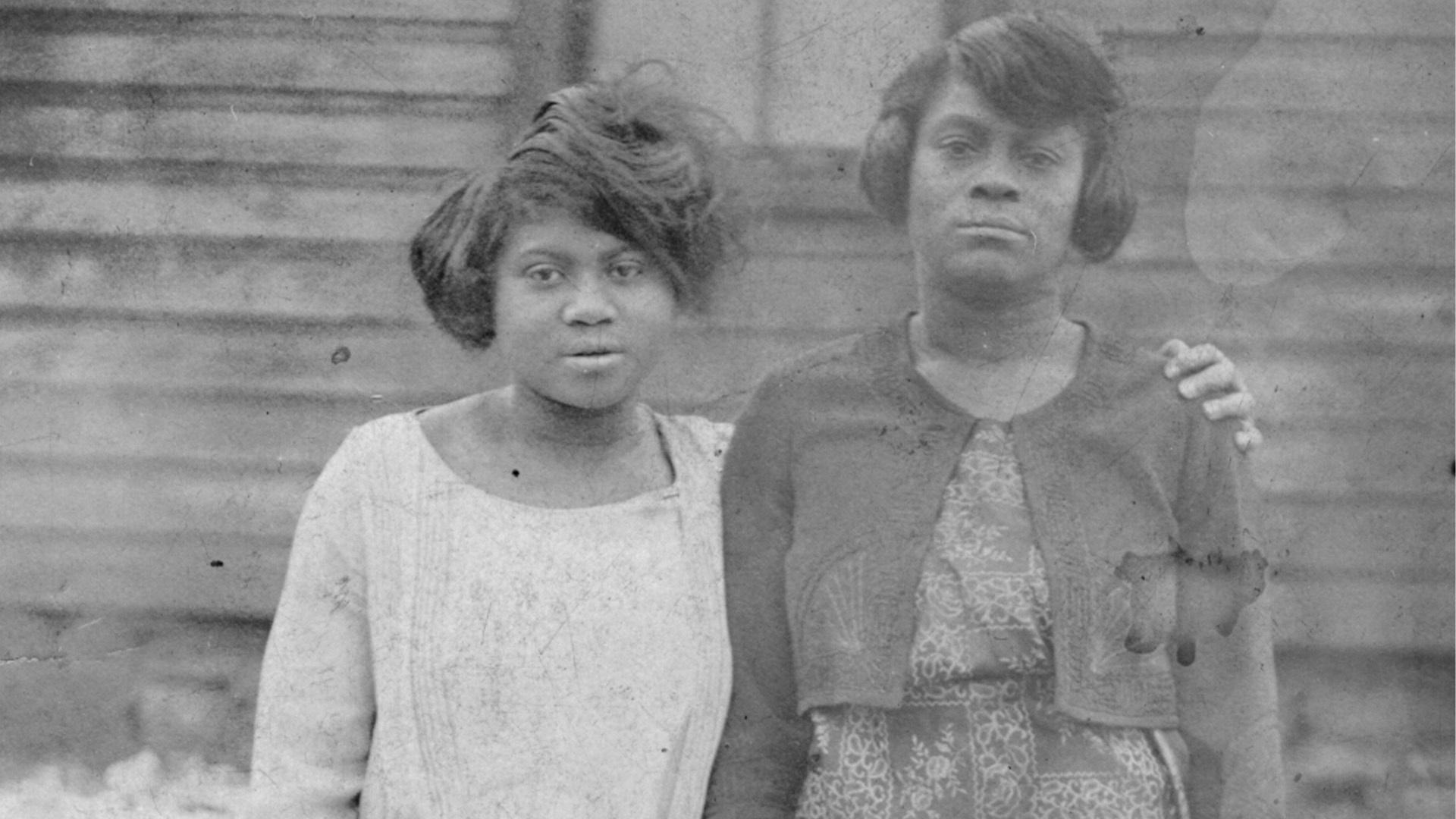 black and white photo of two black women, one with arm around the shoulder of the other