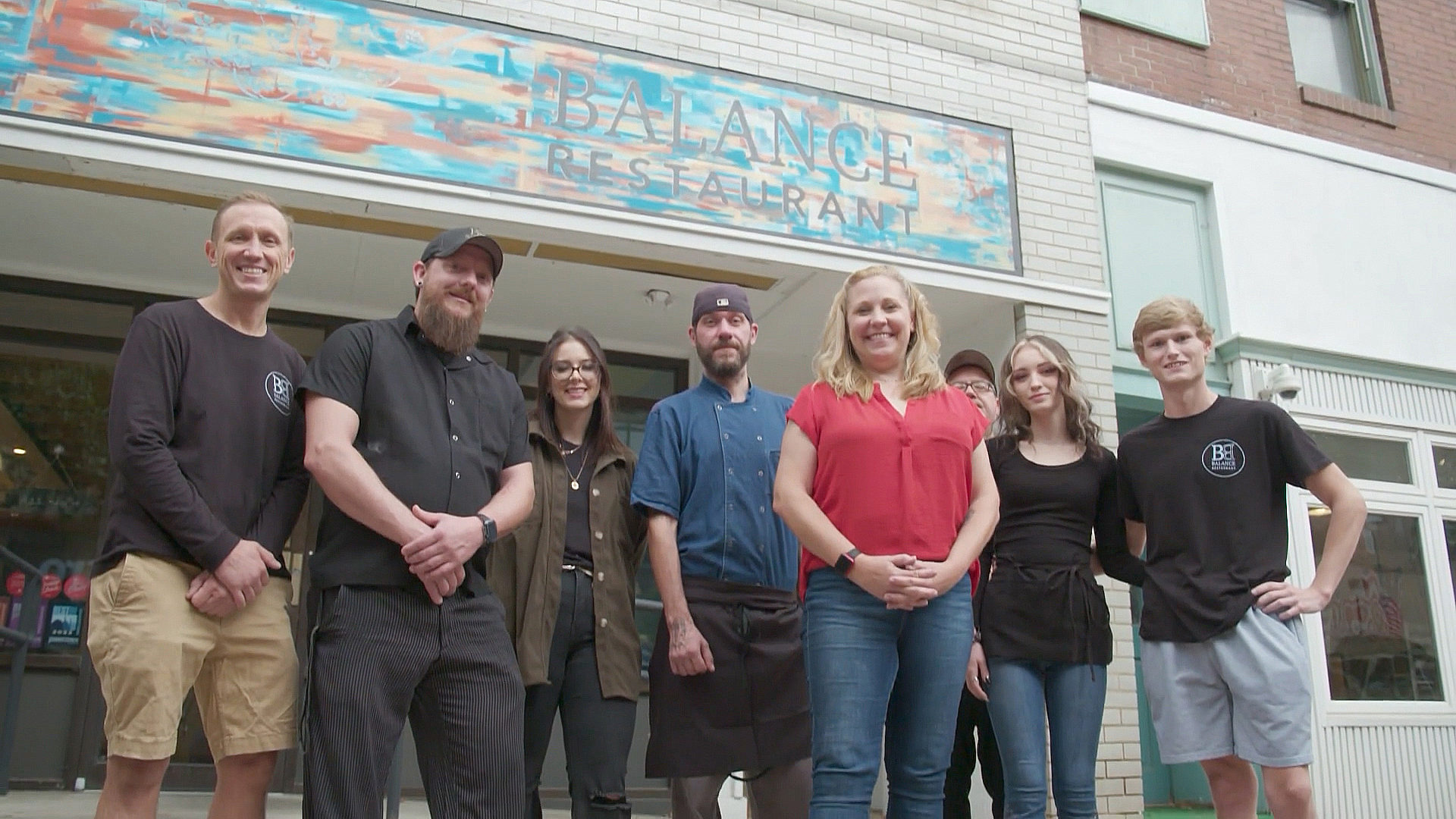 Group of restaurant workers standing in front of restaurant building.