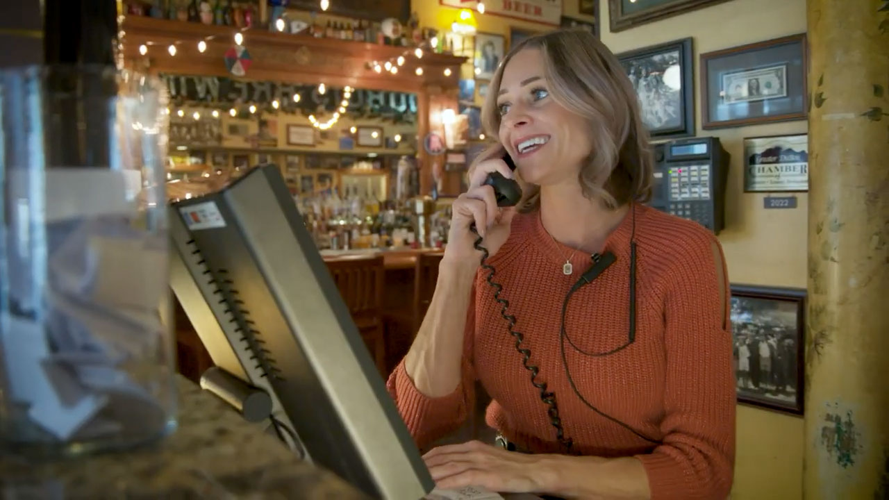 Woman at host desk in restaurant talking on a phone.