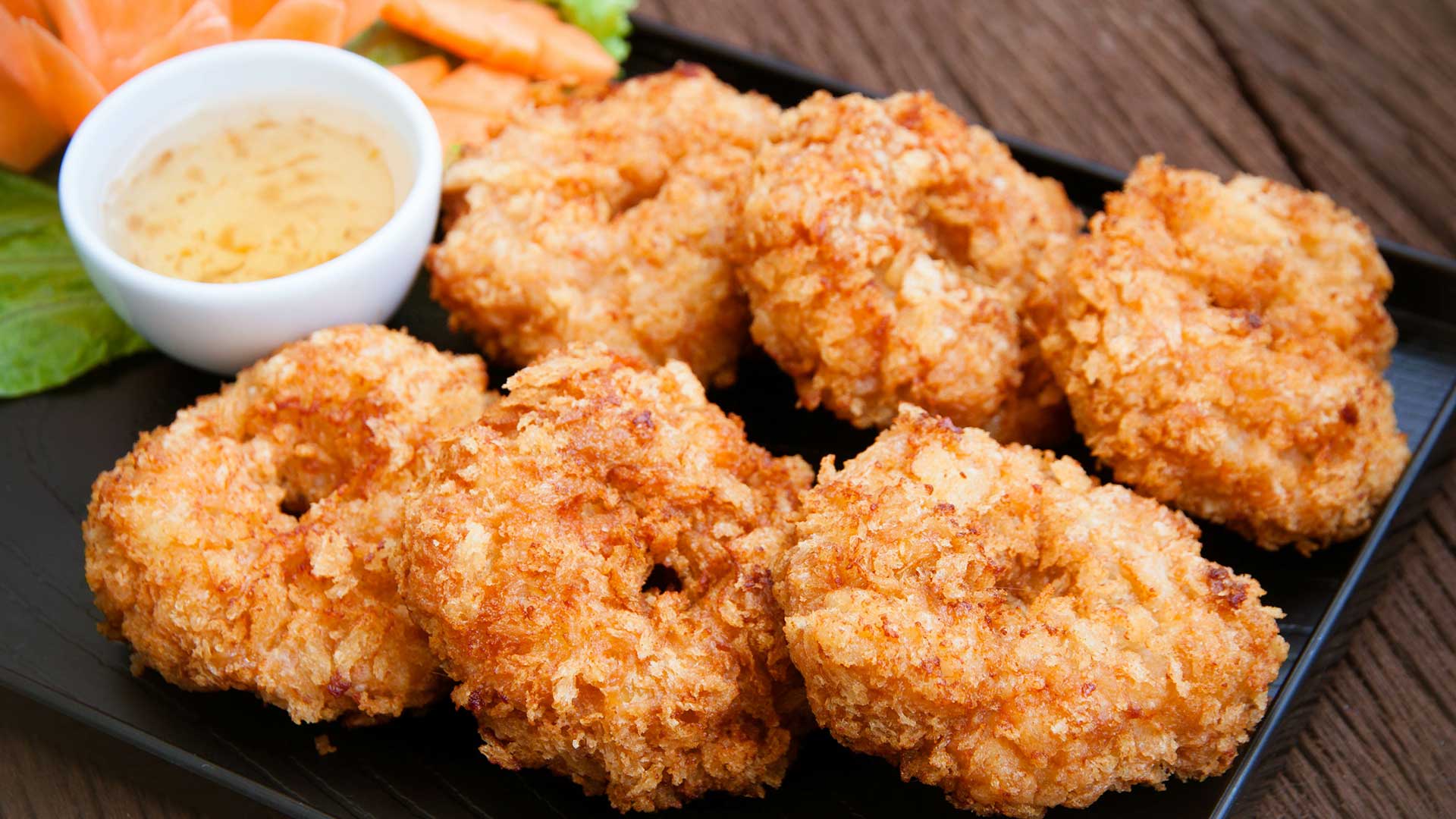 Six pieces of deep fried shrimp on a plate with a bowl of dipping sauce.