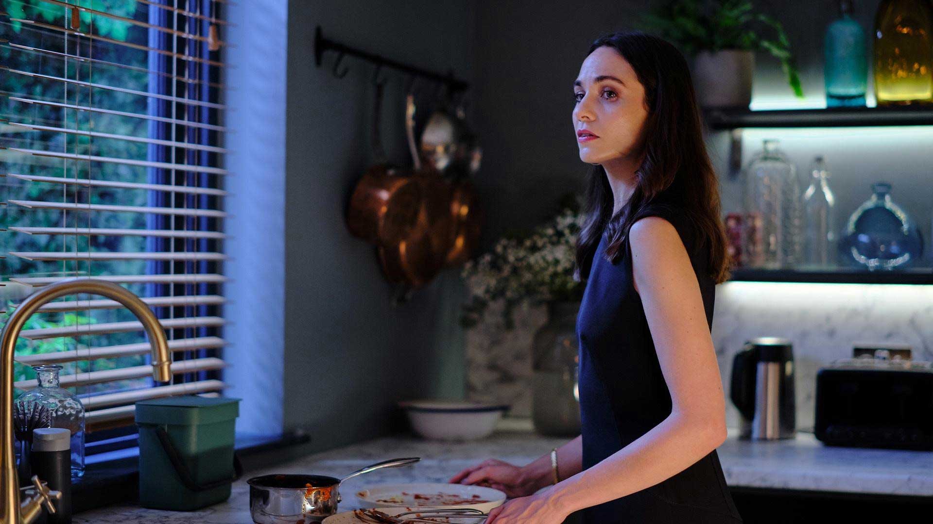 Woman standing near a window in a kitchen.